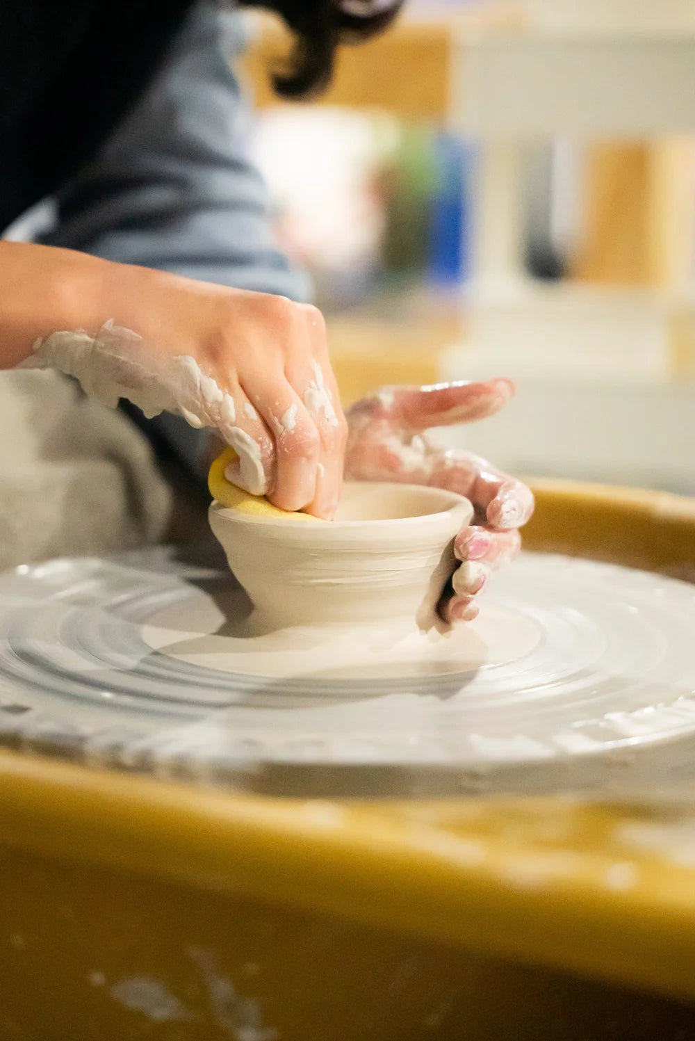Hands shaping clay at a pottery wheel throwing class